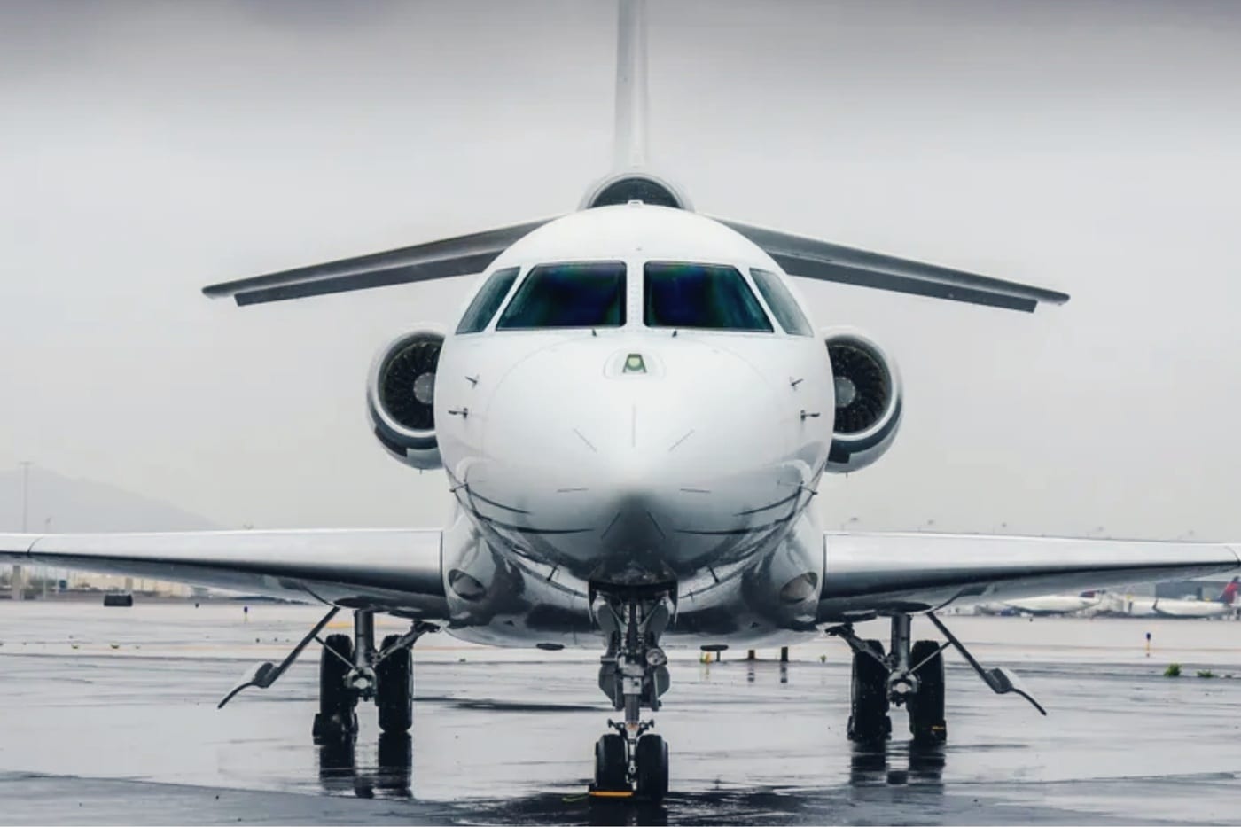 Un jet d’affaires de face sur une aire de trafic mouillée, sous un ciel couvert