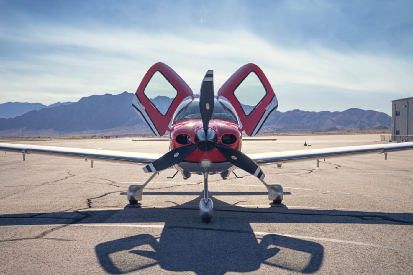 Un avion léger rouge quatre places de face sur une aire désertique, portes papillon ouvertes